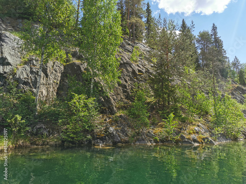 View of the rocky shores and the emerald water of the Marble Canyon in the Ruskeala Mountain Park on a sunny summer day.