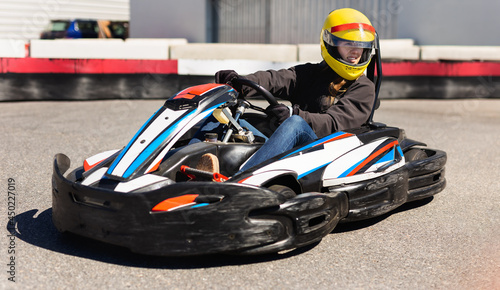 Portrait of girl in helmet driving kart at racing track outdoors