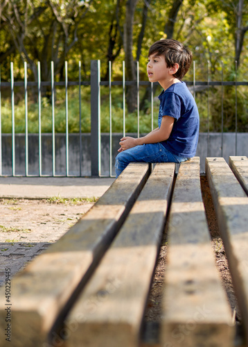 Brunette kid sitting in profile, waiting on a square bench. vertical