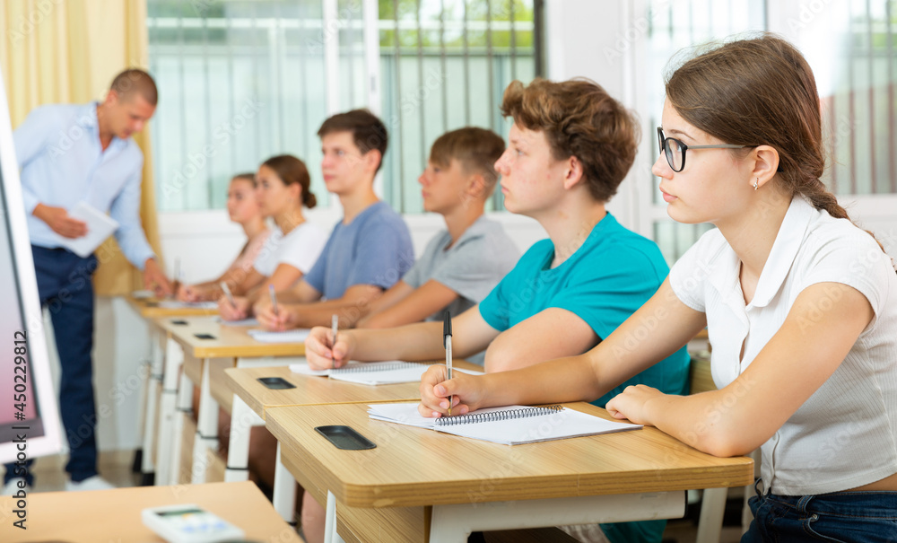 Pupils sitting in class and listening carefully to male teacher.