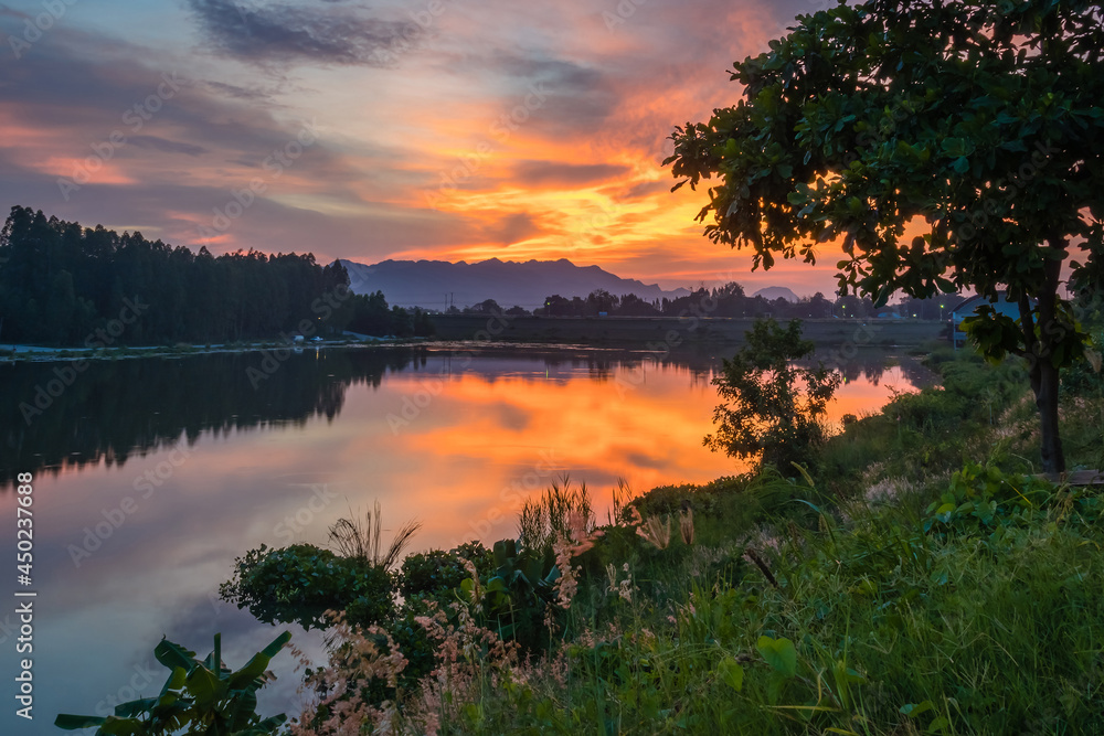 Obraz premium Beautiful view of twilight silhouette sunset on the water reservoir while the sky after sunset has orange light coming out of the clouds and reflecting with the water in the reservoir.