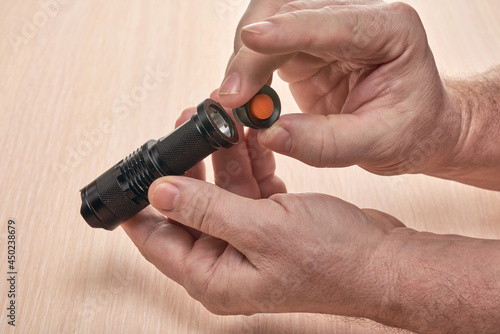Hands hold a small black flashlight and replace the battery in it