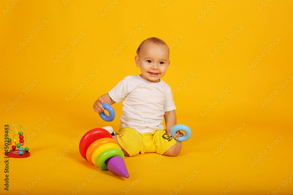 a little boy in a white T-shirt and yellow shorts plays with blocks pyramid toys