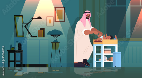 sad arab father changing diaper to his little son fatherhood parenting concept dark night home living room interior