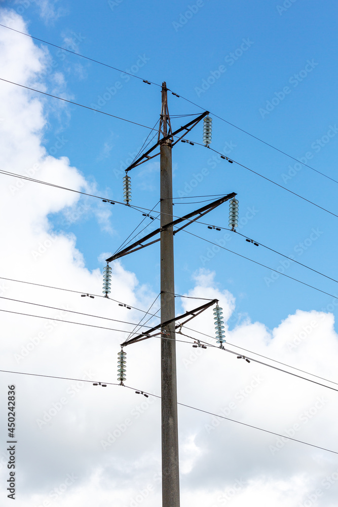 A reinforced concrete pole with insulators and wires on a background of blue sky and clouds. High-voltage line. High voltage A reinforced concrete pole with insulators and wires on a background of blue sky and clouds. High-voltage line. High voltage