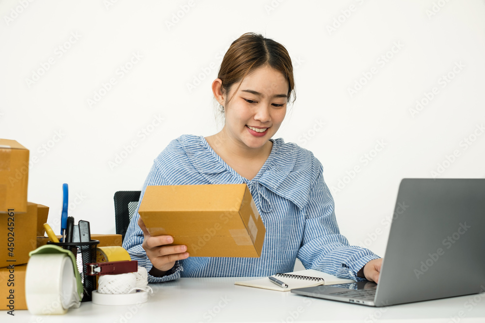 Young Asian woman business owner with many parcel boxes on the table happy online sales job, use the laptop, get an order from customers, take notes, and make arrangements for delivery by post Young Asian woman business owner with many parcel boxes on the table happy online sales job, use the laptop, get an order from customers, take notes, and make arrangements for delivery by post