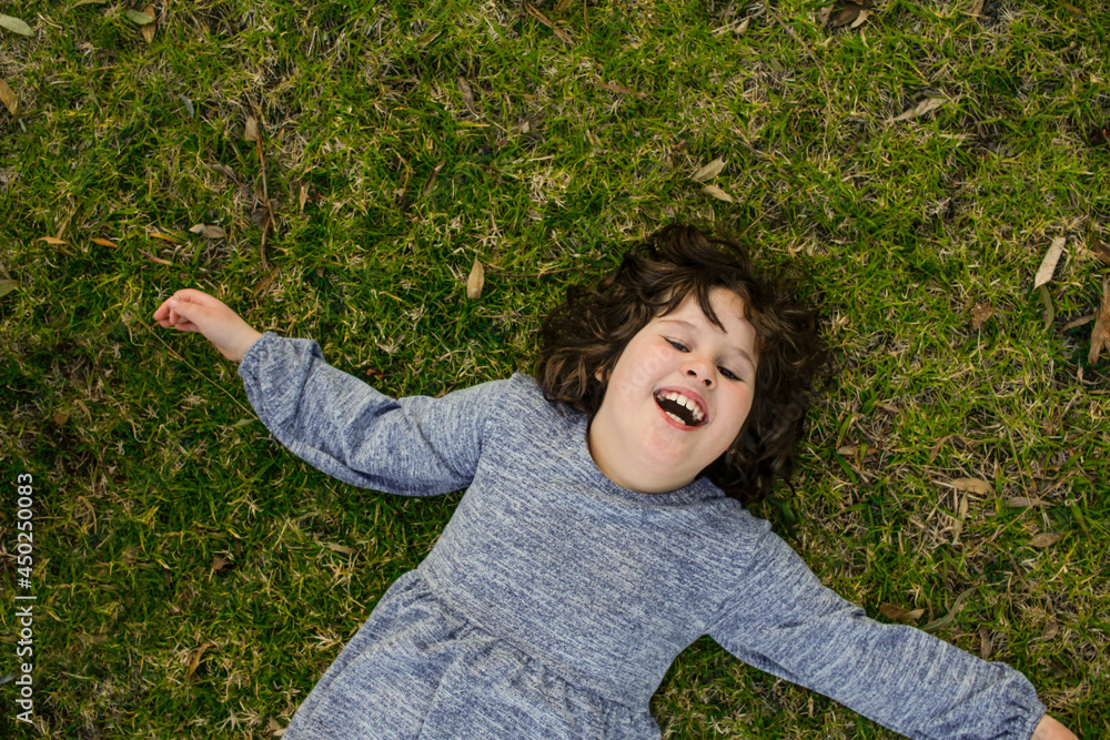 Young girl happily lying on grass with arms spread out Young girl happily lying on grass with arms spread out