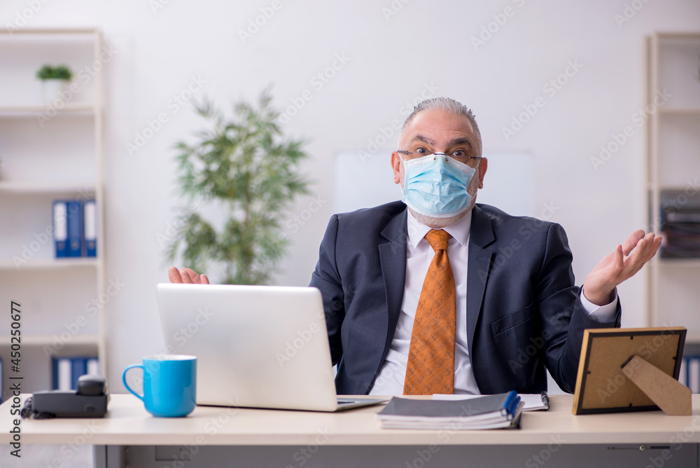 Old male employee working in the office during pandemic Old male employee working in the office during pandemic