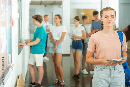 Fototapeta Naklejka Na Ścianę i Meble -  Teenage girl standing in school's hallway. Group of young students standing in line in background.