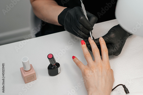 Beautician s salon  manicure  nail painting procedure.A manicurist paints a client s nails with red varnish in a nail salon.