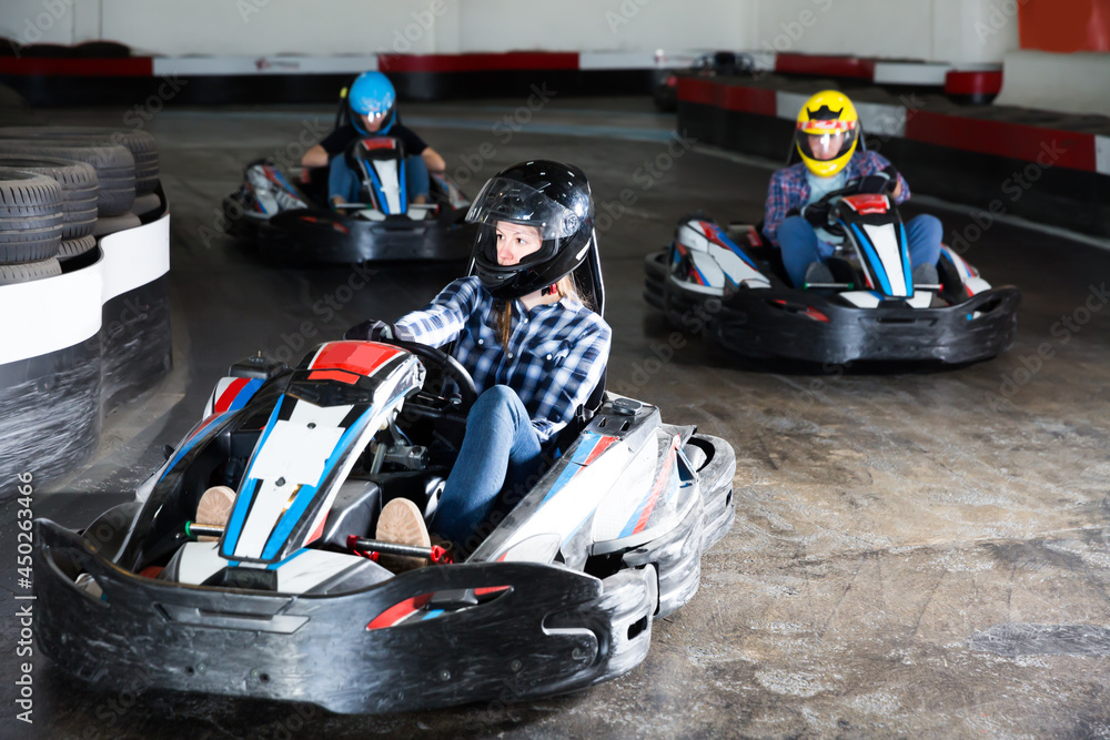 Young people in helmets driving cars for karting in sport club indoor