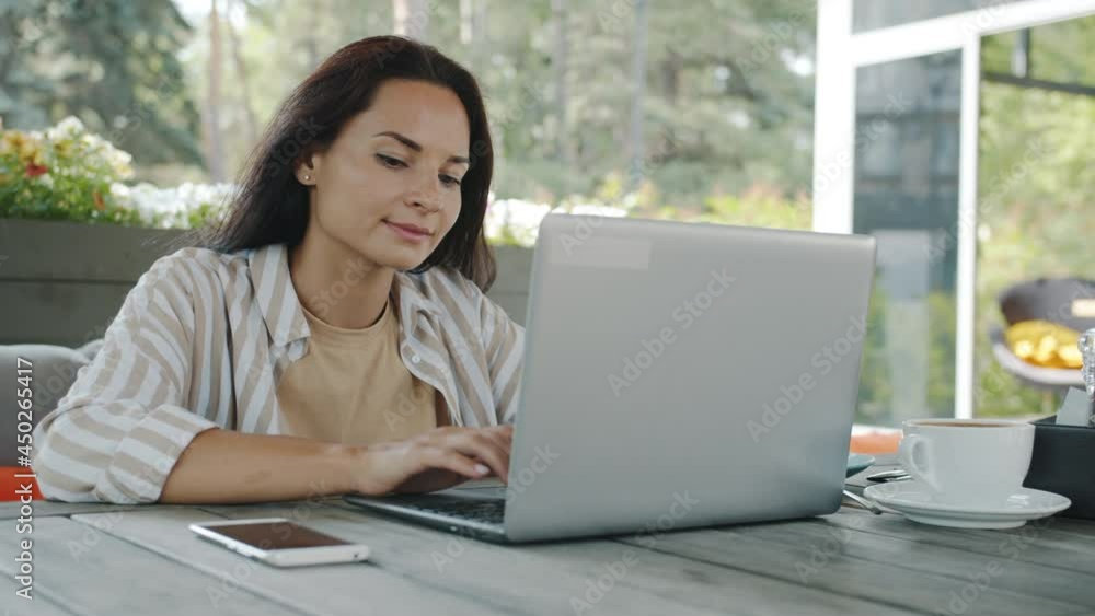 Beautiful young brunette is working with laptop typing enjoying remote job in open air cafe on summer day. Modern technology and freelancers concept. Beautiful young brunette is working with laptop typing enjoying remote job in open air cafe on summer day. Modern technology and freelancers concept.