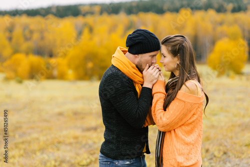 A guy warms the palms of his beloved girl against the background of the autumn landscape. Fall trip at the weekend