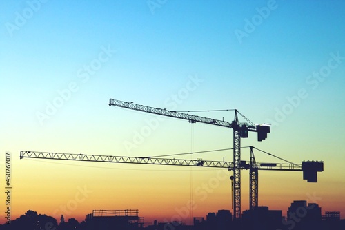 Grúas torre de construcción al atardecer. Silueta de la grúa sobre un bonito fondo naranja y azul con los últimos rayos de sol en Madrid, España. photo