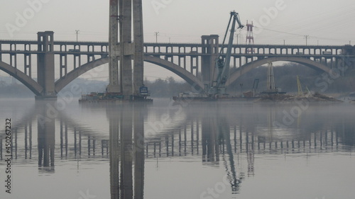 Lustrzane odbicie budowy mostu przez rzekę Dniepr w Zaporożu, Ukraina