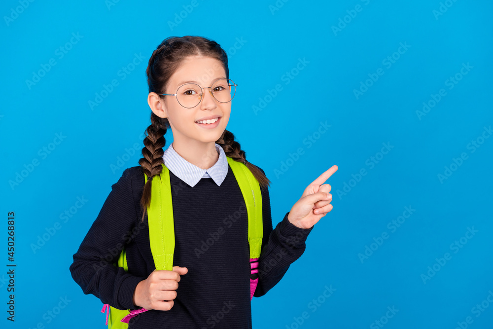 Photo of cheerful good mood schoolgirl point finger copyspace advertise product isolated on blue color background Photo of cheerful good mood schoolgirl point finger copyspace advertise product isolated on blue color background