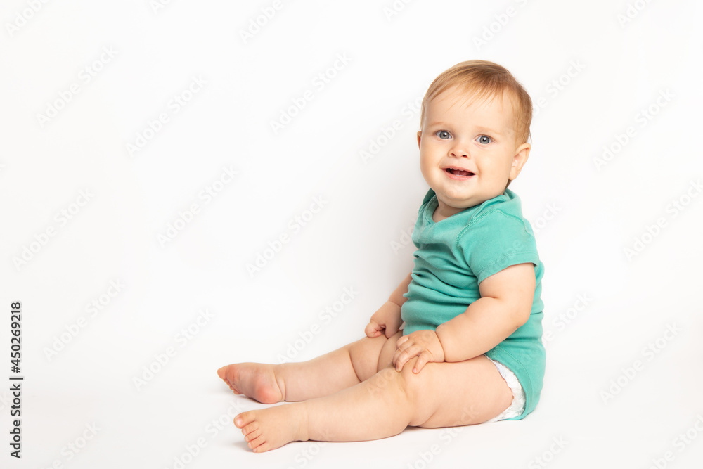 Infant child baby boy wearing green t-shirt laughs happy looking at the camera isolated sitting on a white background. Childcare and upbringing concept. Infant child baby boy wearing green t-shirt laughs happy looking at the camera isolated sitting on a white background. Childcare and upbringing concept.