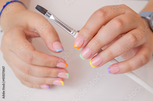 Women s hands with a brush on a white canvas background for drawing. French manicure with a multi-colored coating.