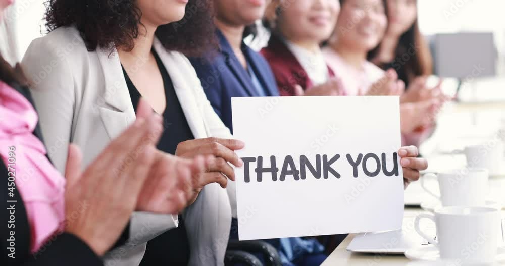 Group of businesswomen sitting at working desk, clapping hands and show thank you word for appreciating to someone in modern office company. Concept of good circumstance in company with colleagues. Group of businesswomen sitting at working desk, clapping hands and show thank you word for appreciating to someone in modern office company. Concept of good circumstance in company with colleagues.