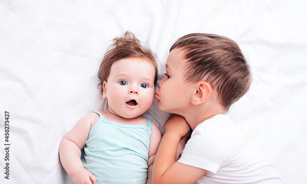 a little beautiful brother kisses his newborn sister on the cheek while lying on the bed a little beautiful brother kisses his newborn sister on the cheek while lying on the bed
