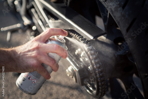 Man's hand using spray can to clean and protect motorbike chain. Concept of maintenance and lubrication of the motorcycle chain.