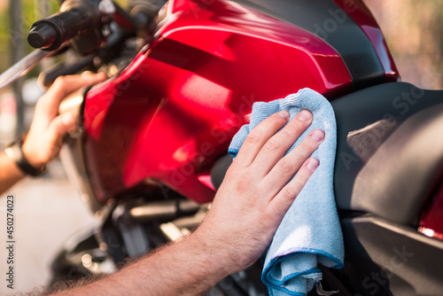 Detail of man cleaning and drying his motorcycle with a microfiber cloth outside.