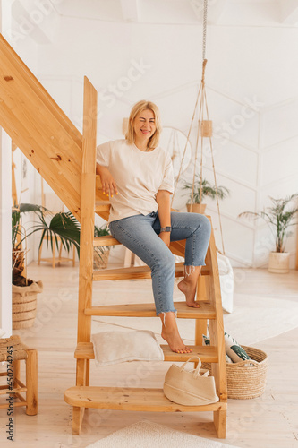 Young woman posing, having fun while sitting on a wooden staircase in a scandinavian style house