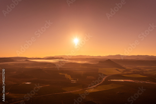 aerial view of a warm sunset over a road between crop fields and mountains