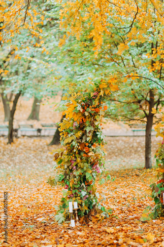 Wedding arch with leaves and flowers in the autumn park.