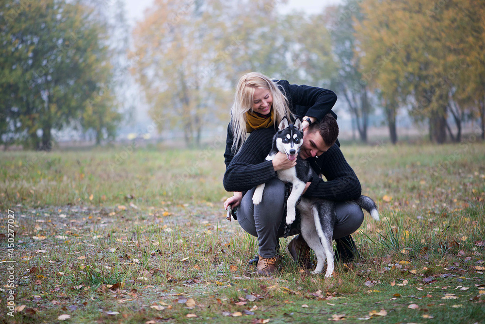 Young family couple with siberian husky dog walking in autumn park