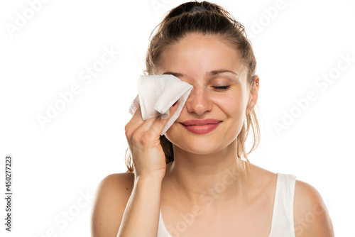 A smiling woman cleans makeup from her face with wet wipe