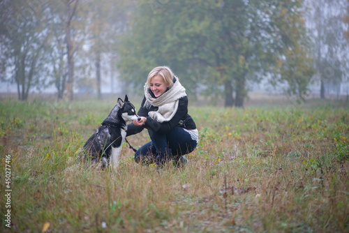 Young woman with beautiful siberian husky dog playing in city park during autumn © Zelma