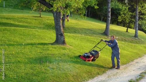 Two men with petrol rotary lawnmowers arranging a meadow between fruit trees. Aerial 4k view. photo