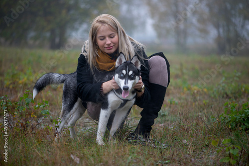 Young woman with beautiful siberian husky dog playing in city park during autumn