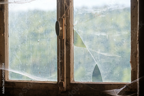 View through a dirty and rusty old broken vintage window with spider web. Seen in Germany in summer.