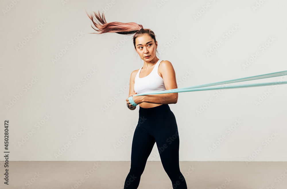 Fototapeta premium Young Asian athlete exercising with a resistance band against white background, looking away