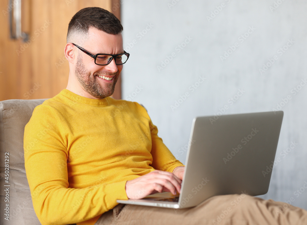 Happy man freelancer dressed casually using laptop while sitting in relaxed pose on sofa at home Happy man freelancer dressed casually using laptop while sitting in relaxed pose on sofa at home