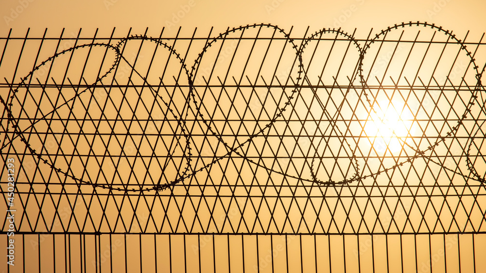 Barbed wire wall against the backdrop of the setting sun. Metaphor of slavery and the search for freedom Barbed wire wall against the backdrop of the setting sun. Metaphor of slavery and the search for freedom