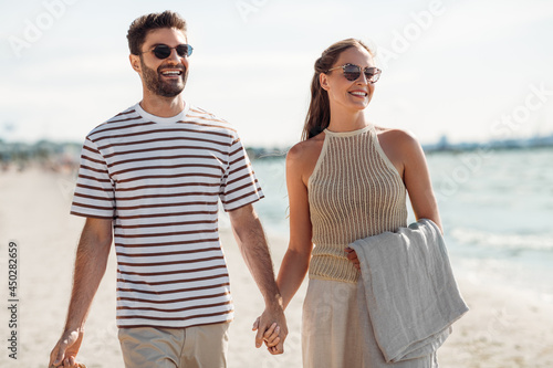 leisure, relationships and people concept - happy couple with blanket walking along summer beach