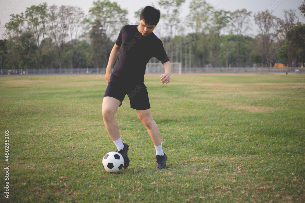 Sports and recreation concept a male soccer player wearing black t-shirt and pants practicing kicking the ball in the grassy field Sports and recreation concept a male soccer player wearing black t-shirt and pants practicing kicking the ball in the grassy field