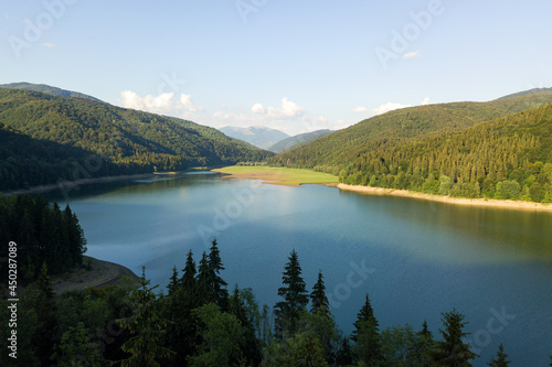 Aerial view of big lake with clear blue water between high mountain hills covered with dense evergreen forest.