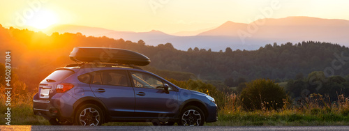 SUV car with roof rack luggage container for off road travelling parked at roadside at sunset.