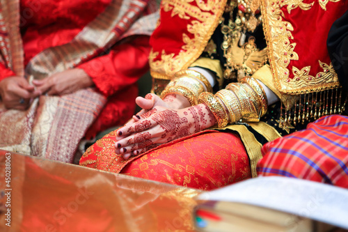Close up hands and nails of Asian Muslim bride with henna paint tattoo and jewelry in a wedding ceremony. Traditional Minangkabau culture heritage from West Sumatra, Indonesia.  © Luthfi Syahwal