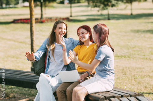 A group of teenage girls is sitting on a park bench and preparing for classes together, discussing homework and having fun. Time together, friends, friendship, training