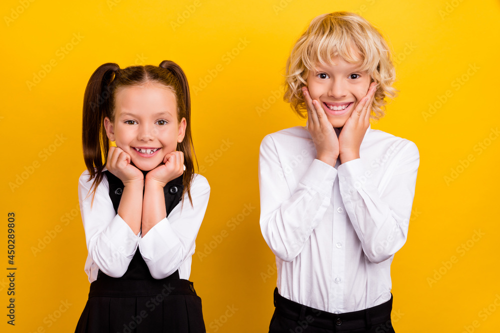 Photo of two classmate schoolkids hands cheeks toothy smile wear school uniform isolated yellow color background Photo of two classmate schoolkids hands cheeks toothy smile wear school uniform isolated yellow color background