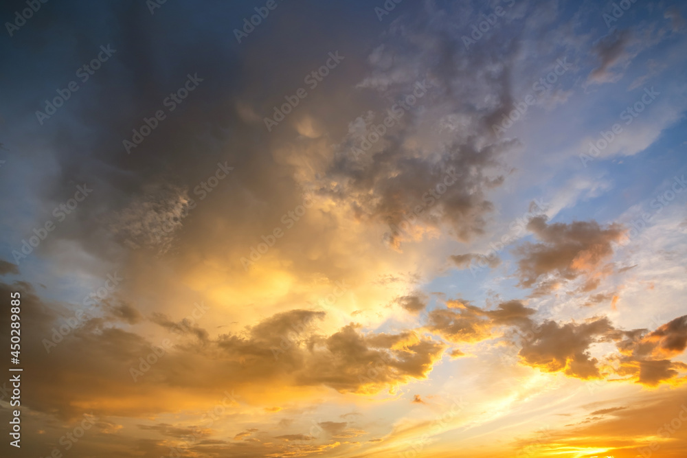 Dramatic sunset sky landscape with puffy clouds lit by orange setting sun and blue heavens.