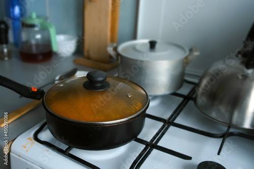 Kettle, pot and frying pan on the gas stove in the kitchen, cooking at home. Everyday life of usual people in third world country. Old time kitchen utensils.