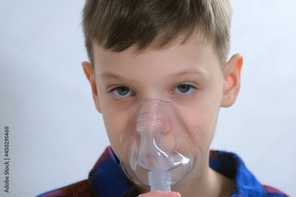 Portrait of child teen boy is breathing in mask using nebulizer for inhalation procedure at home. Fibrosis, covid-19, asthma, copd. Treatment, cure and procedure. Using inhaler for therapy.
