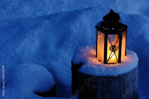 Christmas candle lantern in snow at dusk.