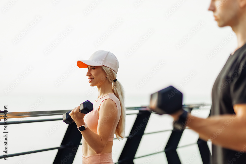 Young sportive fitness couple, man and woman in sportswear working out outdoors, sportive couple training with dumbbells